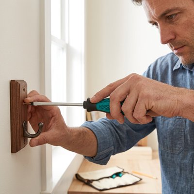 monsieur fixant un support de vetement sur un mur avec un Tournevis