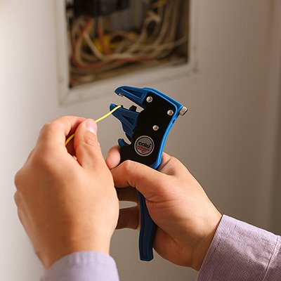 Pince a denuder noir et bleu dans une main avec un fil électrique dans l'autre