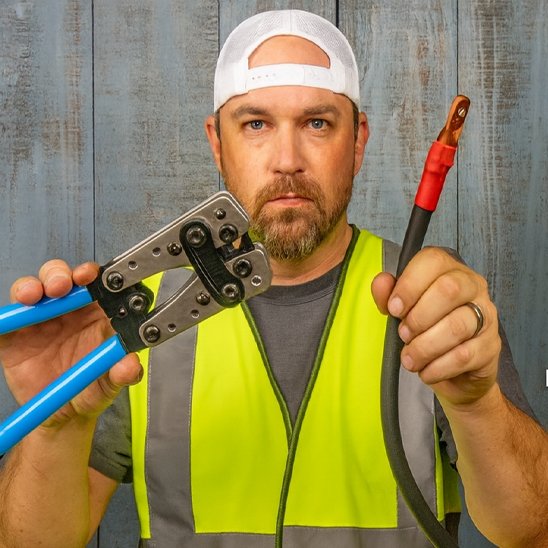 Pince a sertir​ dans la main d'un homme avec un cable electrique rouge dans l'autre main