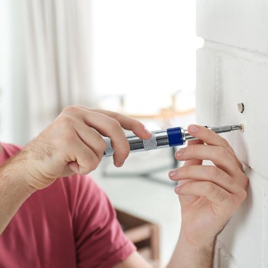Tournevis dans la main d'un homme fixant un vis dans le mur