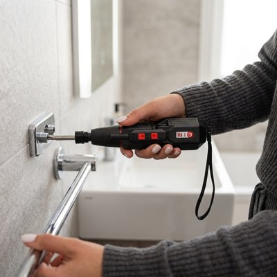 Tournevis électrique dans la main d'un homme fixant un support de serviette dans une salle de bain